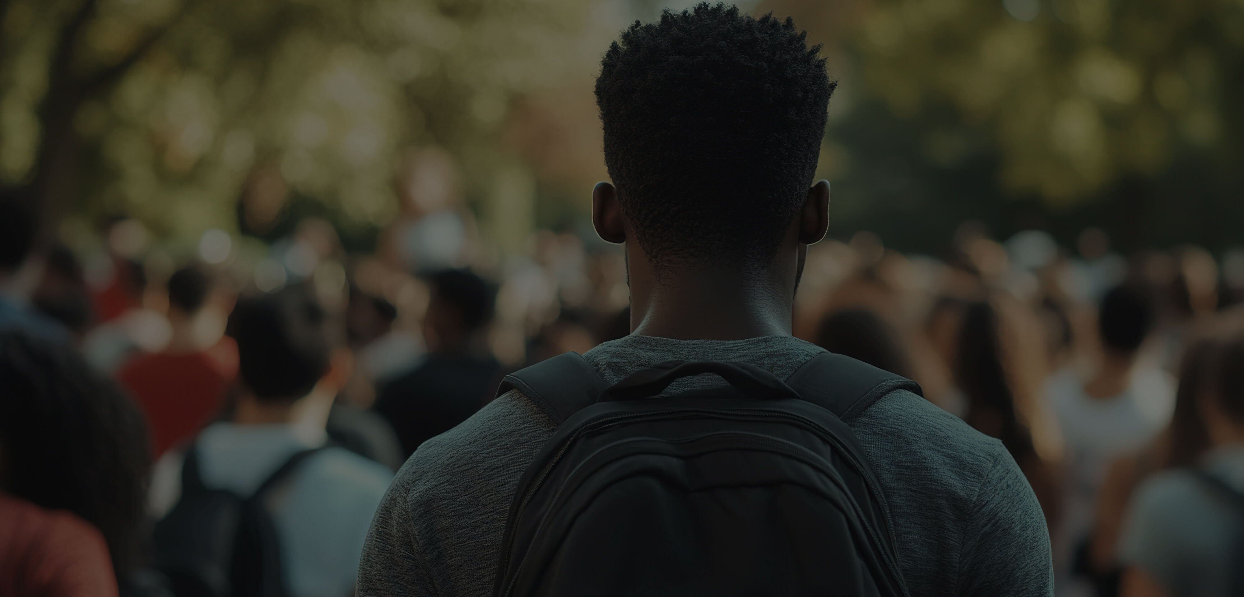 Young adult heading to college, part of a large crowd wearing a school backpack.